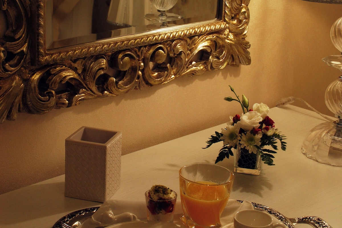 A tray with food and drinks, a mirror with an ornate frame, and a vase with flowers.