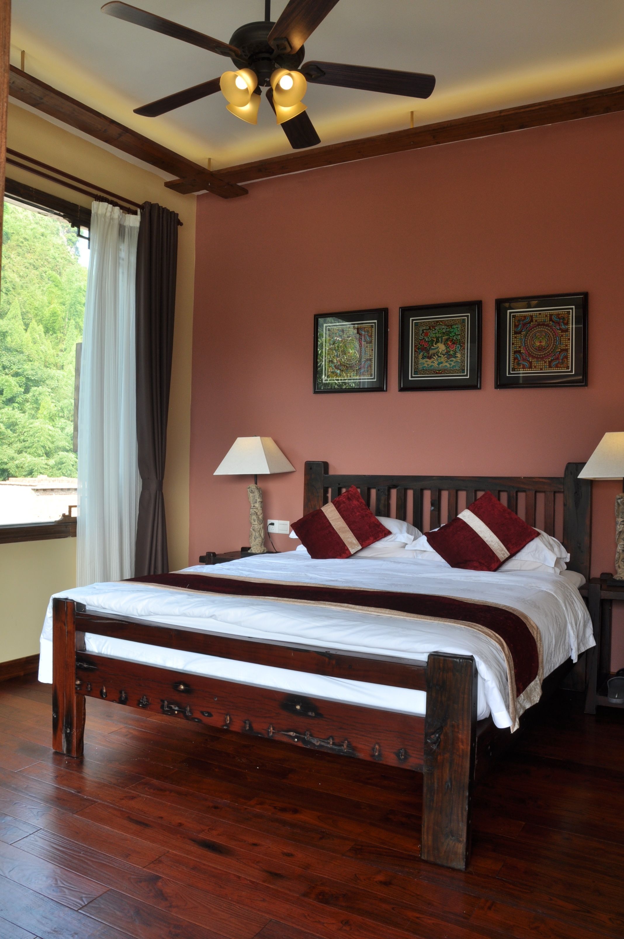 A bedroom with a wooden bed, a ceiling fan, and three framed artworks on the wall.