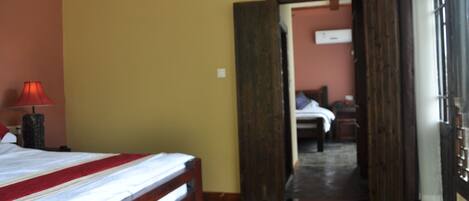 Una habitación de hotel con una cama de madera, una lámpara roja y vistas a otra habitación por una puerta abierta.