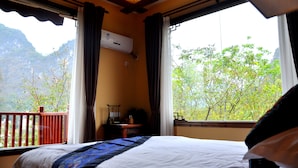 Ein Hotelzimmer mit Bett, Nachttisch, Klimaanlage und Blick auf Grünflächen und Berge.