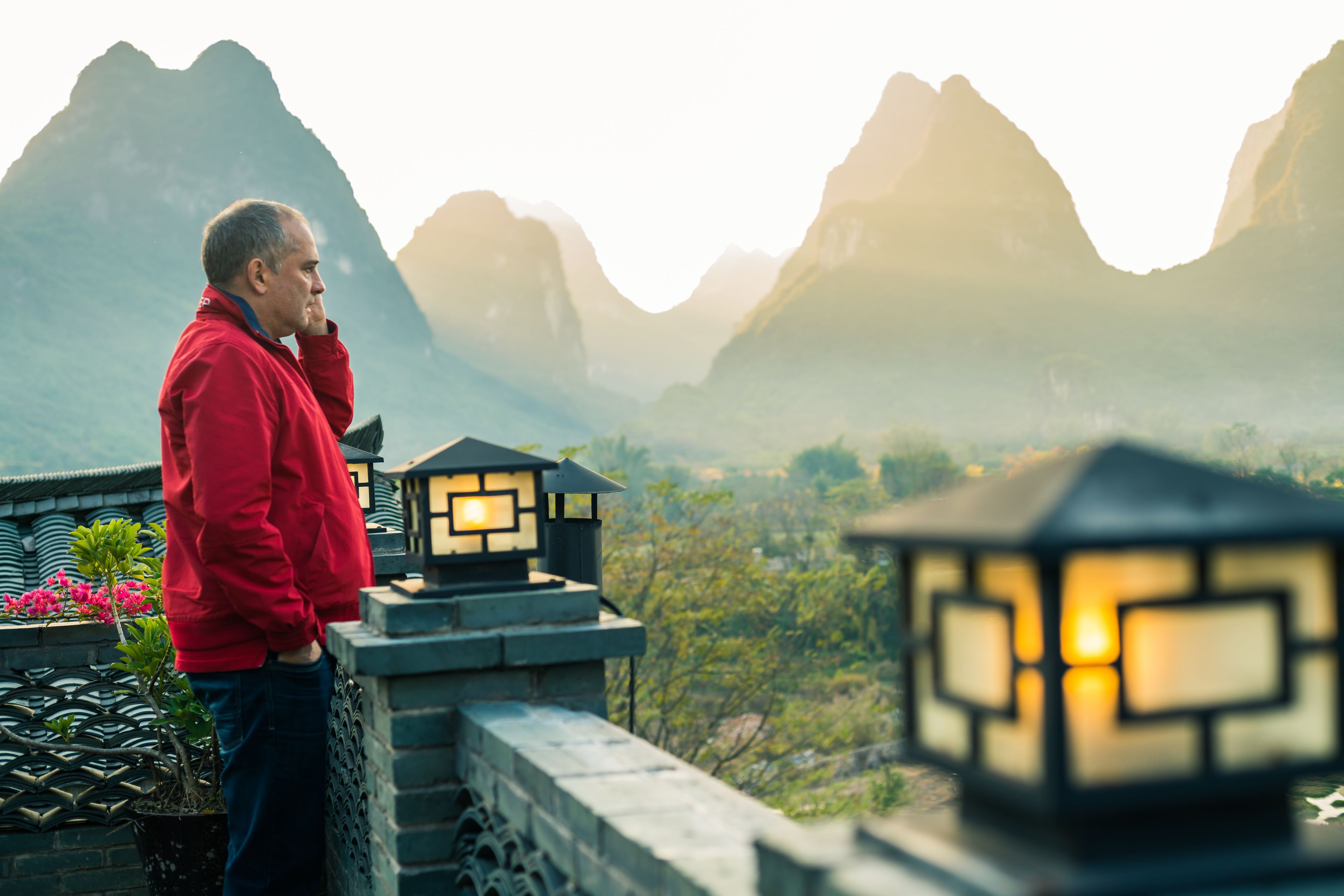 A person standing on a balcony overlooking a mountainous landscape with traditional lanterns.