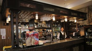Angolo bar con una macchina da caffè, scaffali pieni di bottiglie e bicchieri appesi.