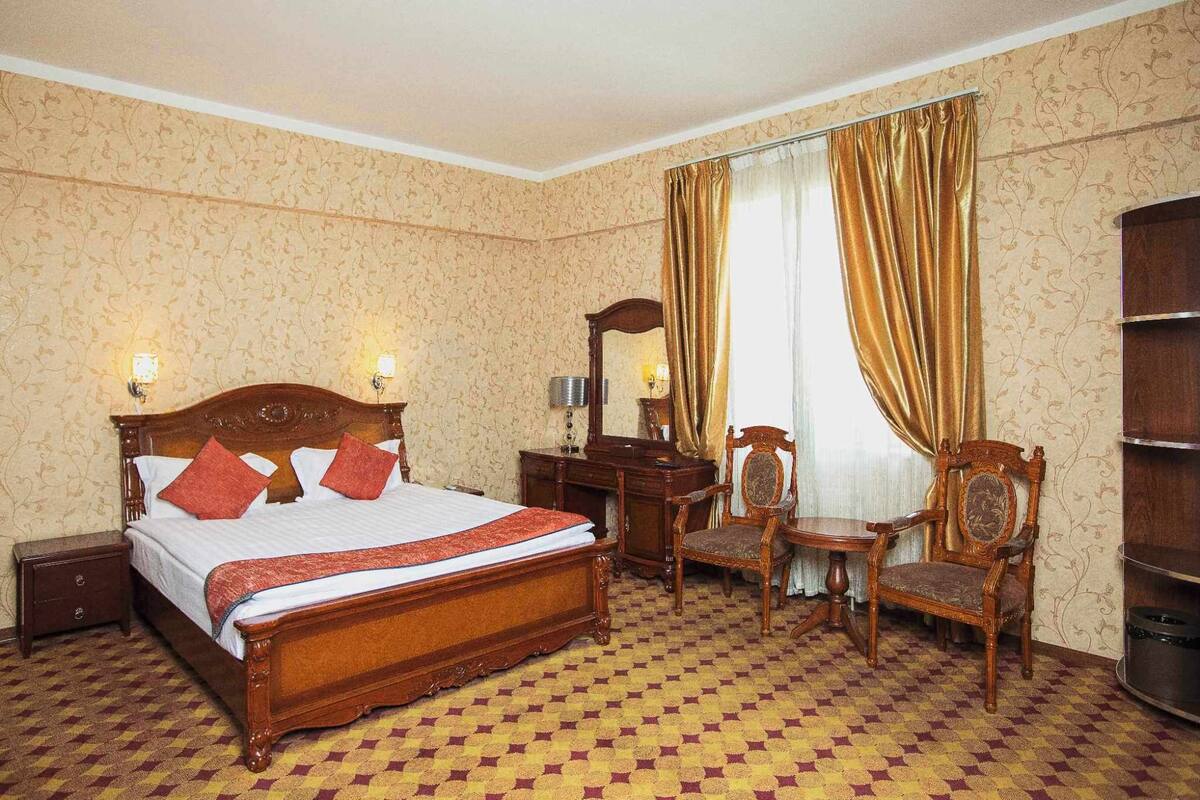 Habitación de hotel con cama, mesita de noche, silla, escritorio y espejo de madera.