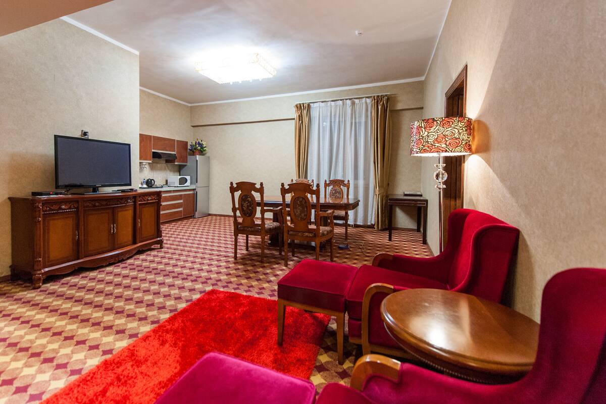 Una sala de estar con televisor, muebles de madera, alfombra roja y un comedor.