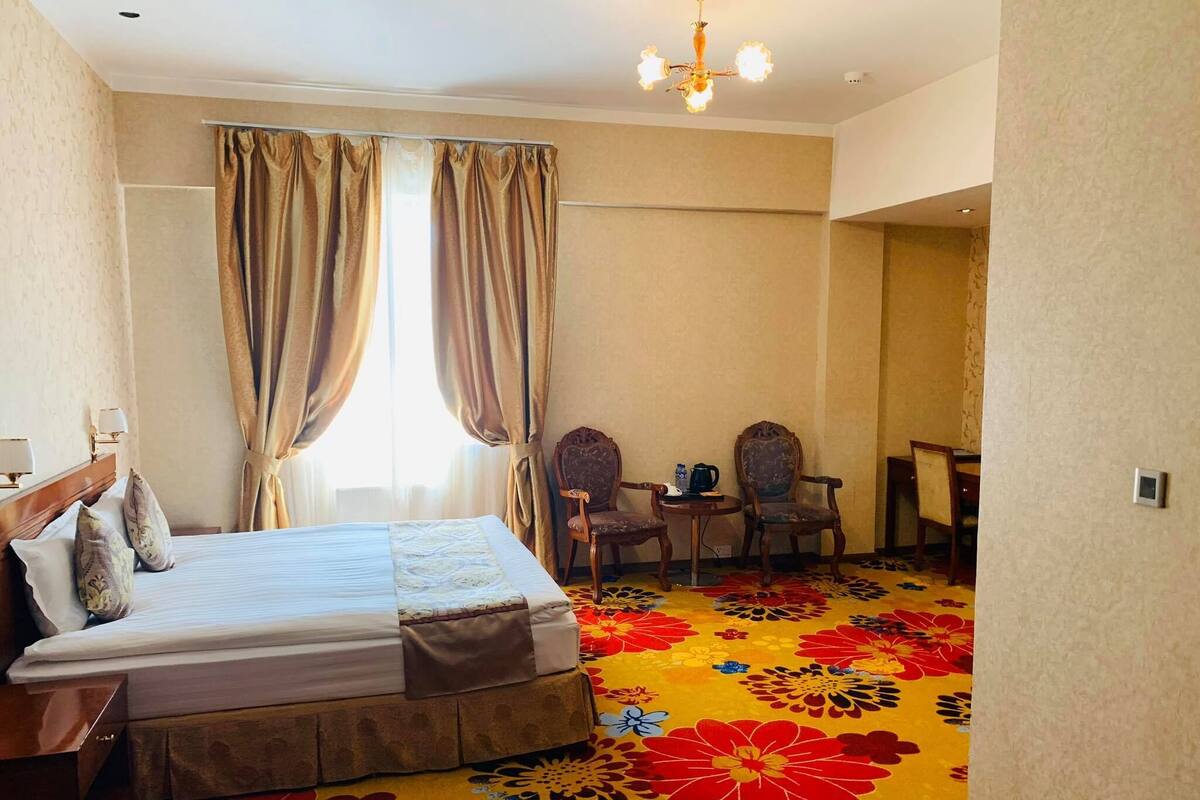 Habitación de hotel con cama, dos sillas, una mesita y alfombra estampada.