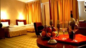 Una camera d'albergo con tappeto a scacchi, due letti, un tavolo da pranzo con candele, frutta e bicchieri da vino.