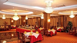 Una sala da banchetto con tavoli rotondi, tovaglie rosse e lampadari.