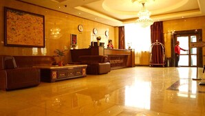 Un'area della reception di un hotel, con scrivania, receptionist, orologio e lampadario.