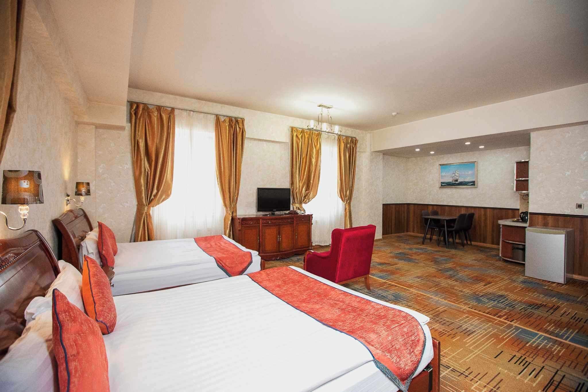 A hotel room with two beds, a desk, a chair, a television, and a small kitchenette.