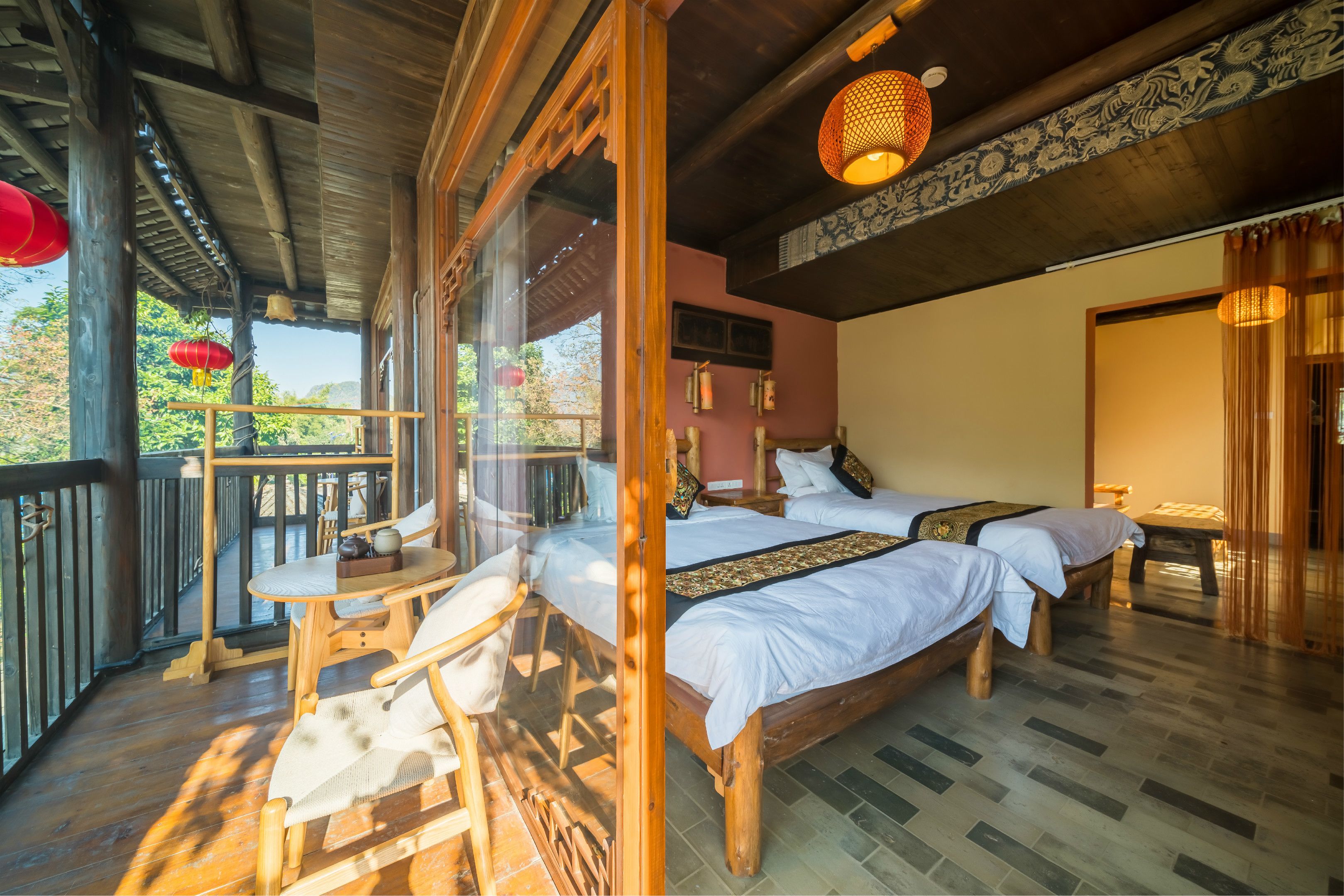 A traditional wooden room with two beds, a balcony, and a view of the outdoors.