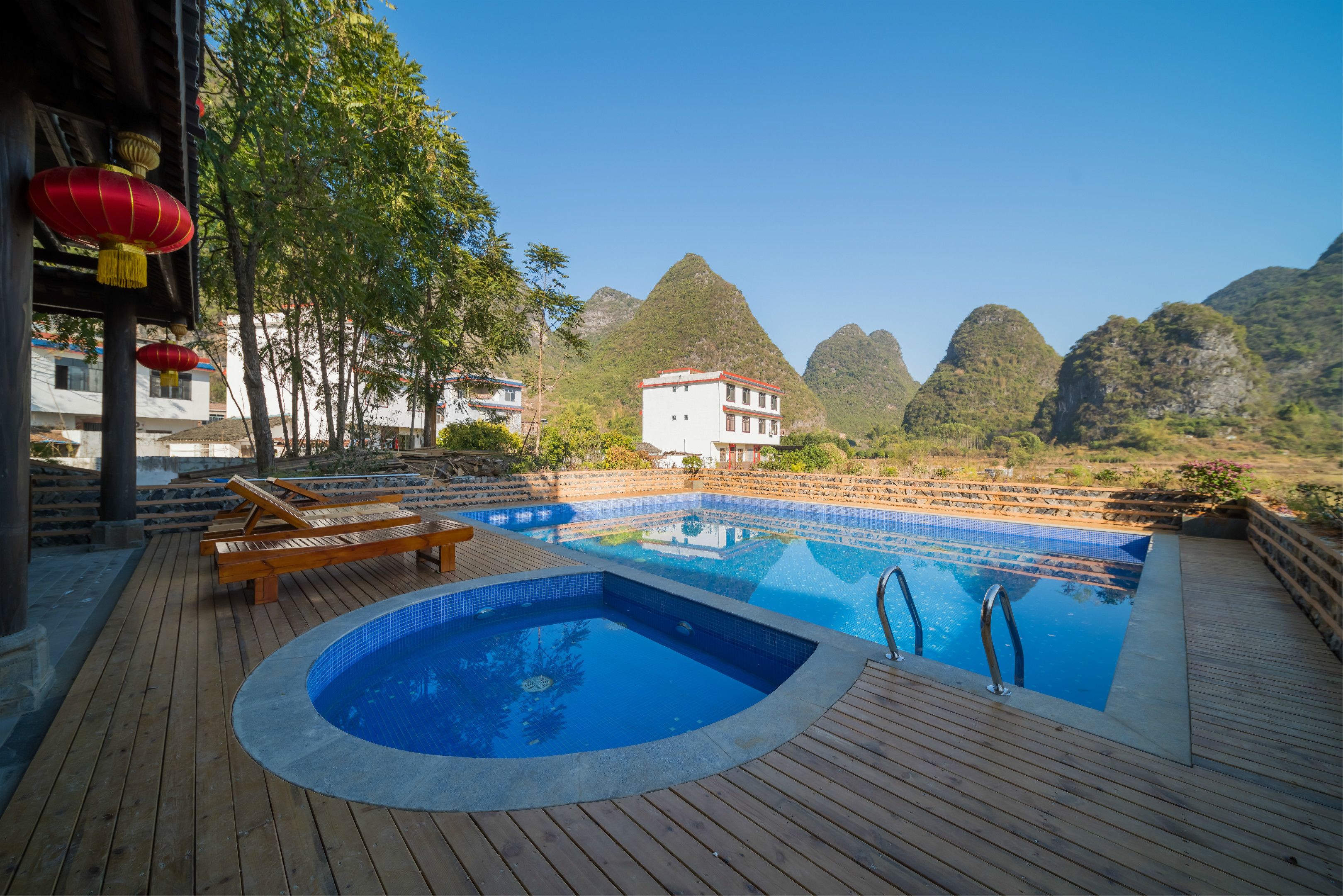 A wooden deck with a hot tub and lounge chairs, a pool, and a view of mountains.