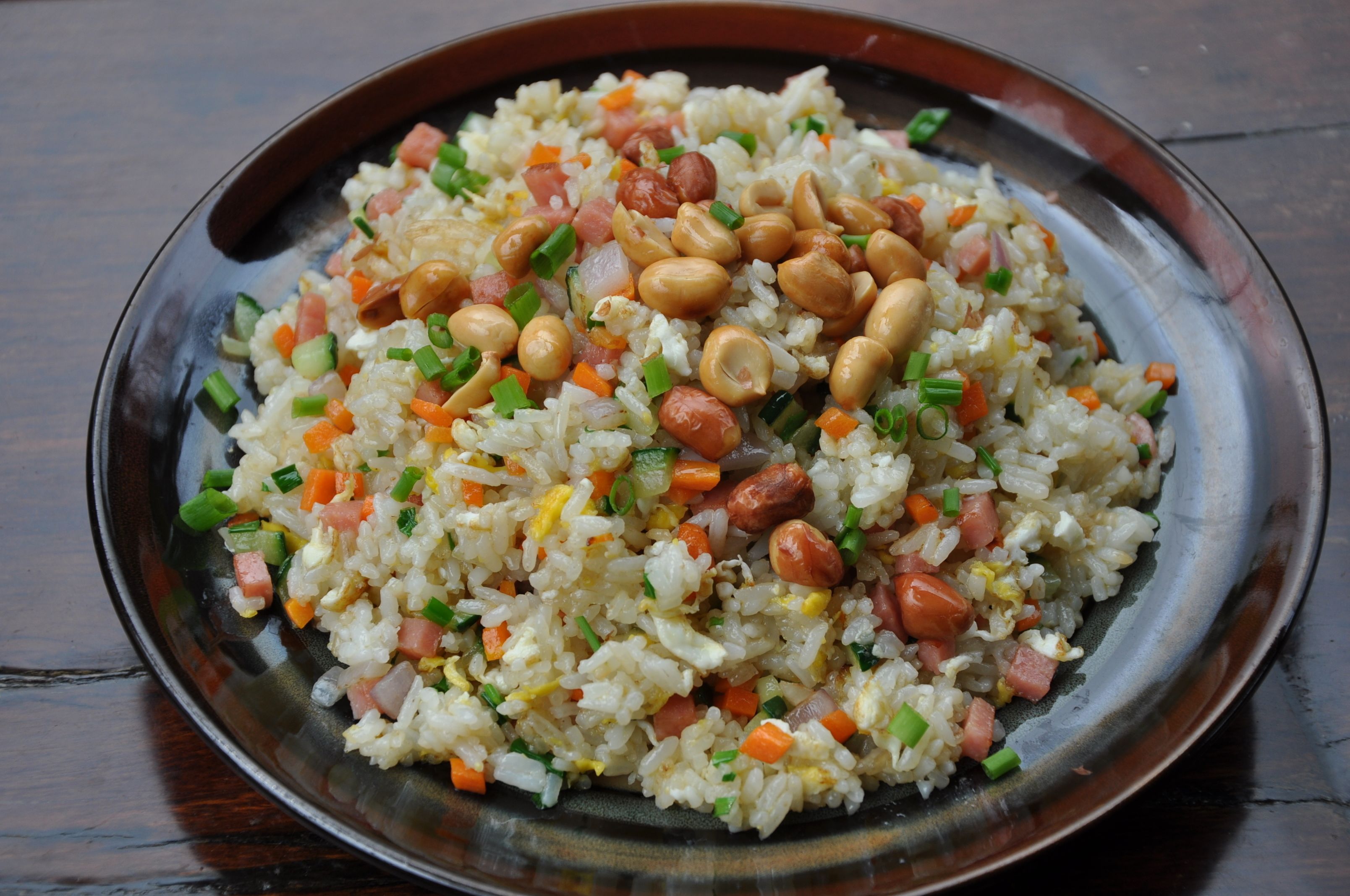 A plate of fried rice with peanuts, carrots, and green onions.