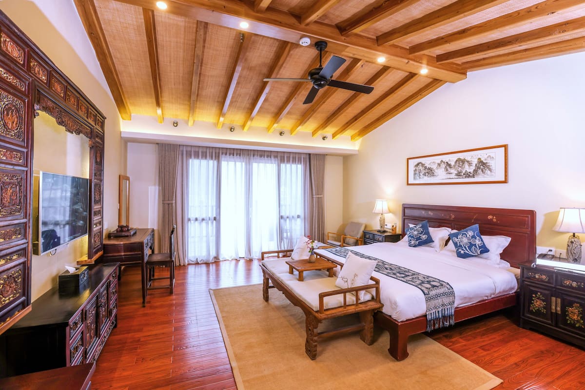 A spacious bedroom with a large bed, wooden furniture, a ceiling fan, and a painting on the wall.