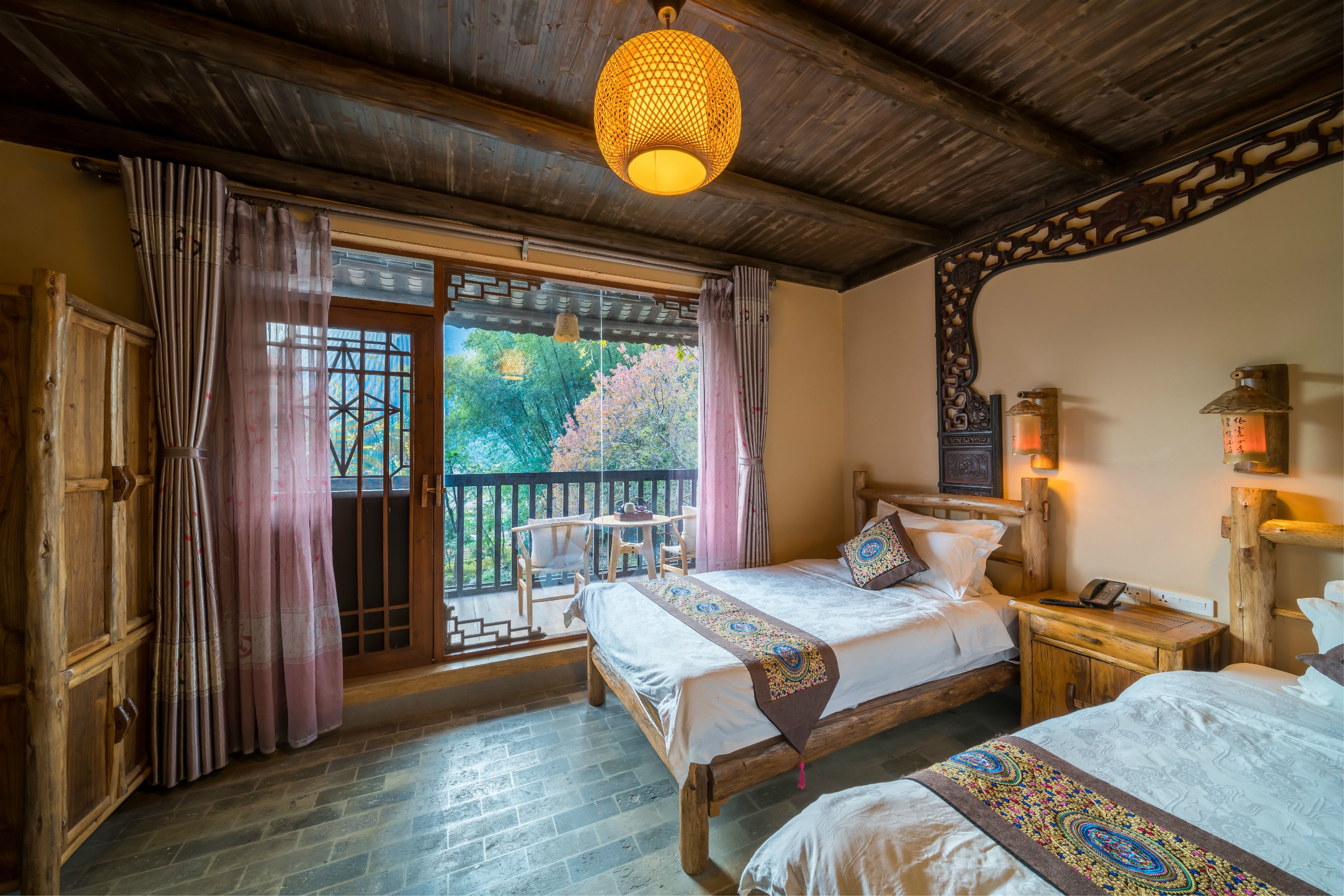 A traditional wooden room with two beds, a balcony with a view of cherry blossoms, and a hanging lantern.