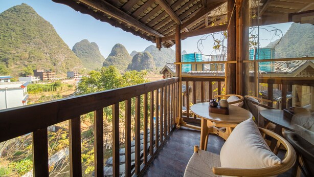 Ein Holzbalkon mit Blick auf Berge, ein Tisch mit Stühlen und eine hängende Leuchte.