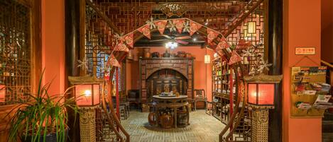 A traditional interior with a central wooden table, bookshelves, and a decorative archway.