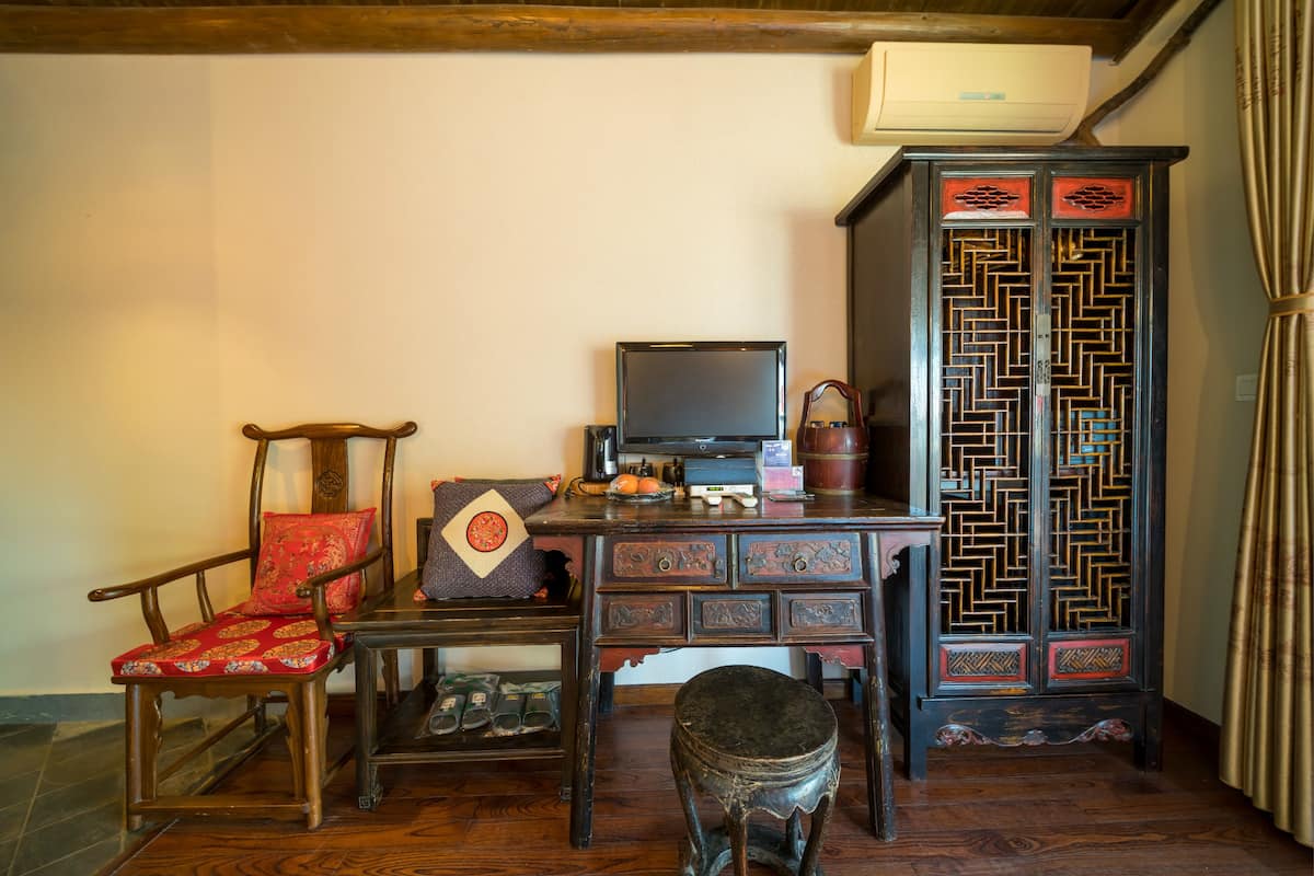 A traditional room with a wooden desk, a television, a decorative cabinet, and a chair with a cushion.