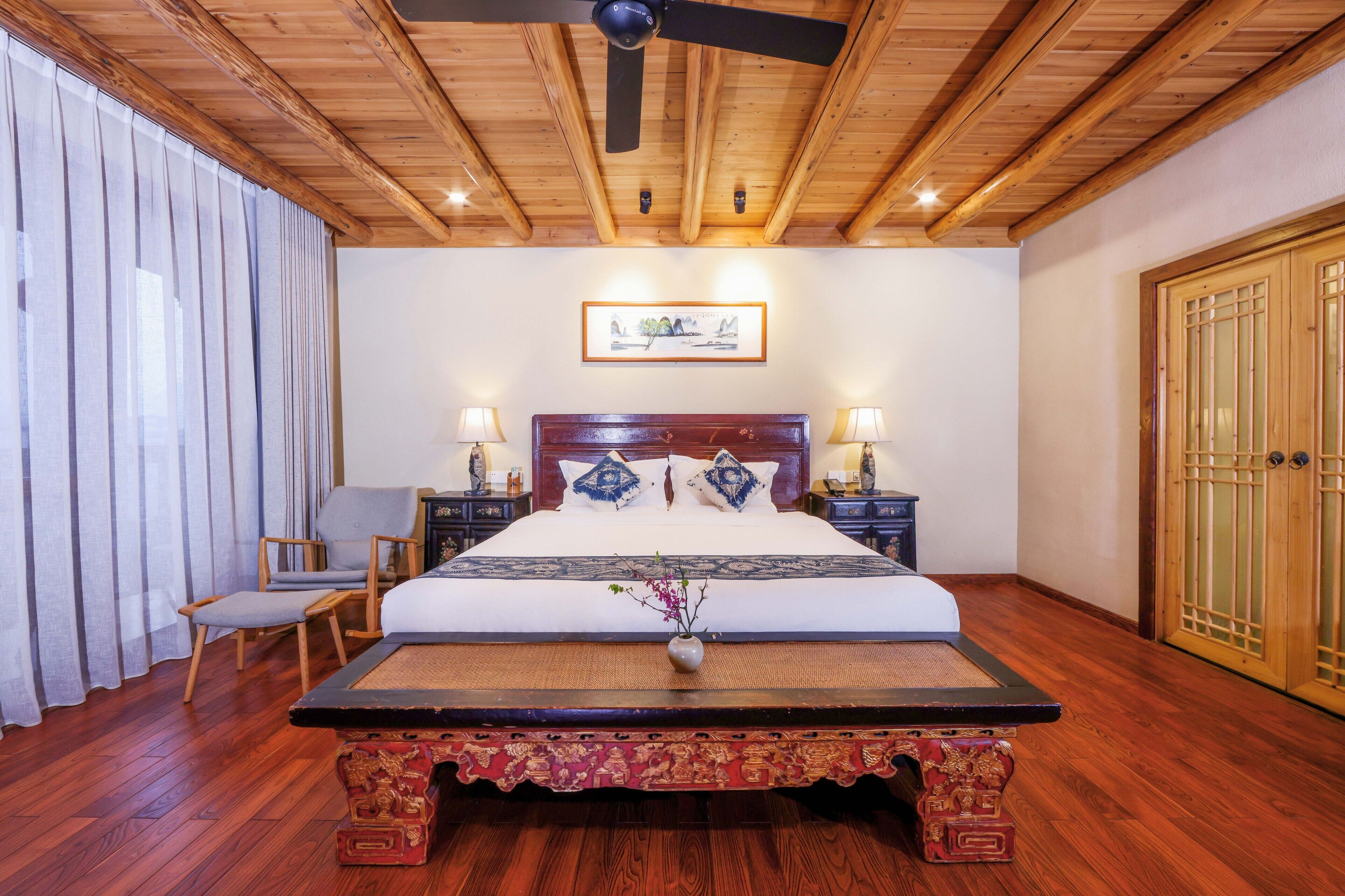 Un dormitorio tradicional de madera con una cama, mesitas de noche, una silla y un banco decorativo.