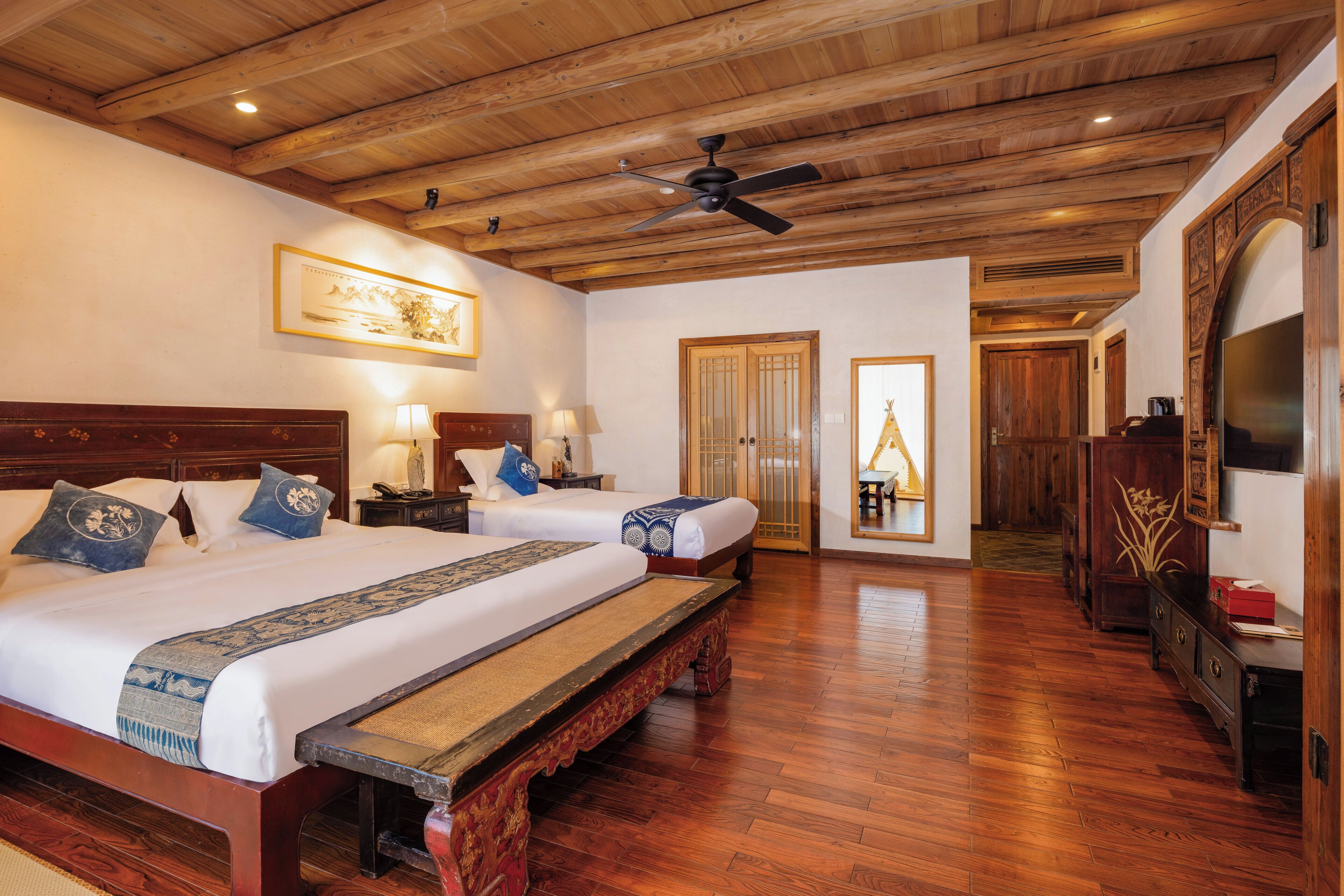 Un dormitorio amplio con dos camas, suelo de madera, ventilador de techo y decoración de estilo tradicional.