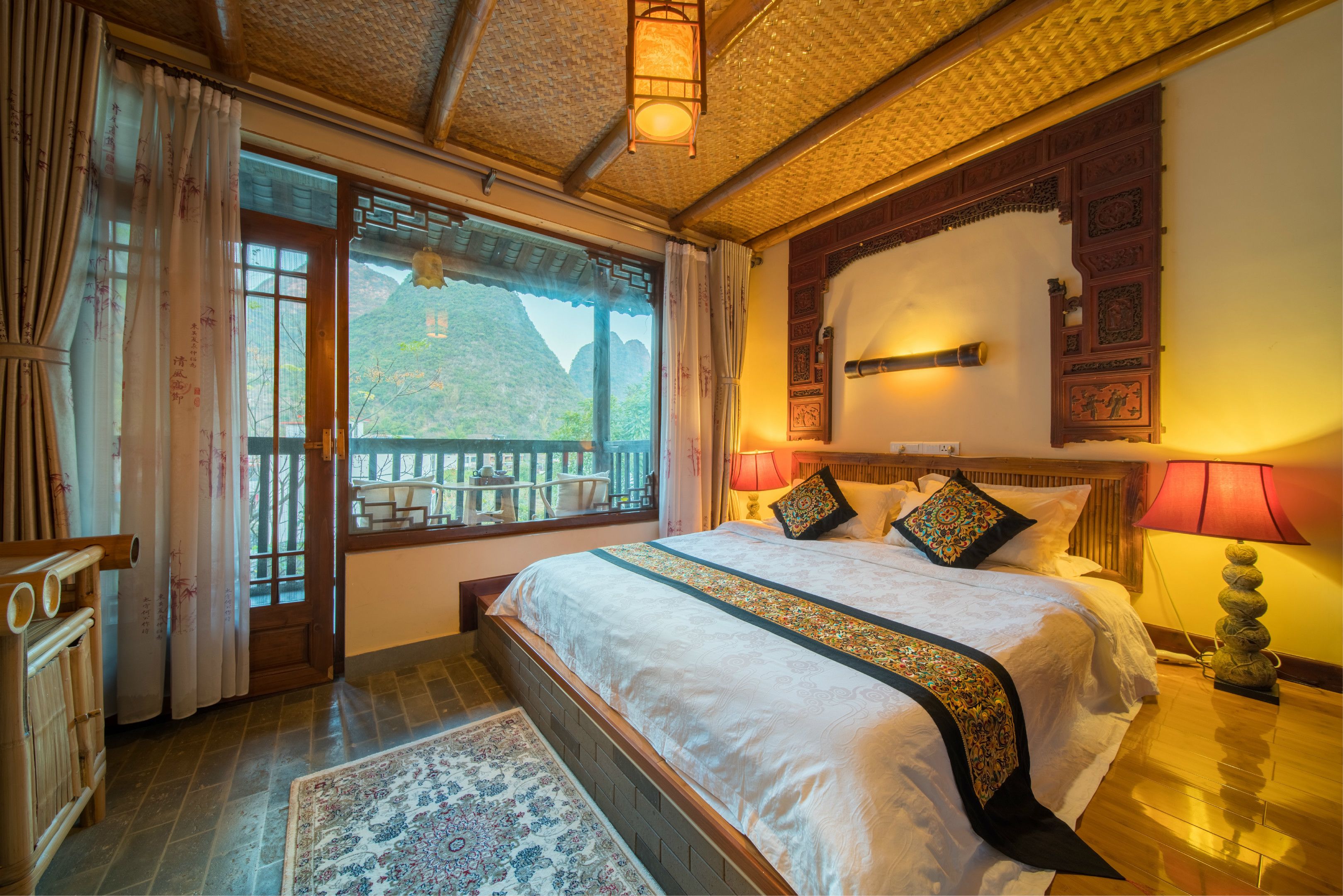 A traditional-style bedroom with a large bed, wooden headboard, and a view of mountains through the window.