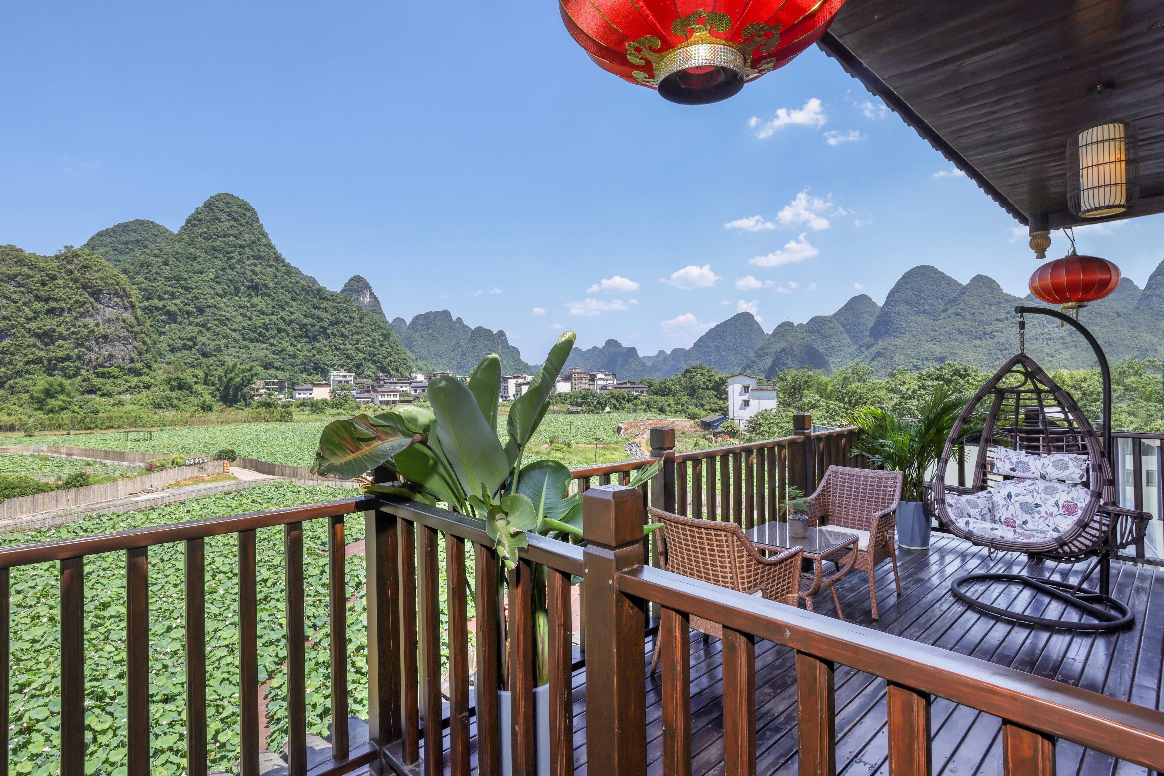 A wooden deck with wicker furniture and a hanging chair, overlooking a lush green landscape and mountains.