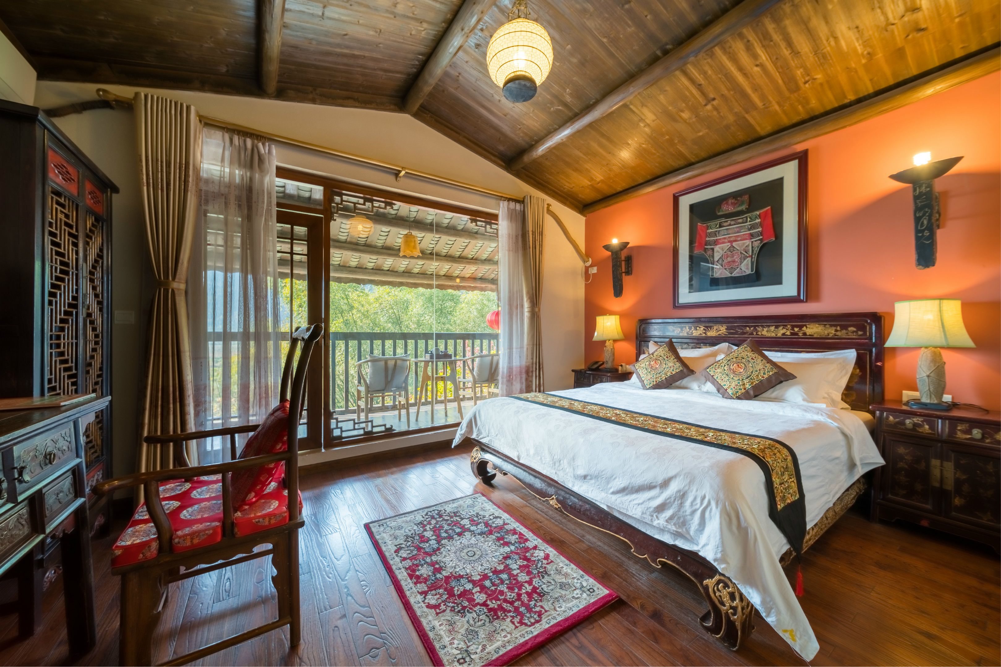 A traditional room with a large bed, wooden furniture, and a balcony with chairs.