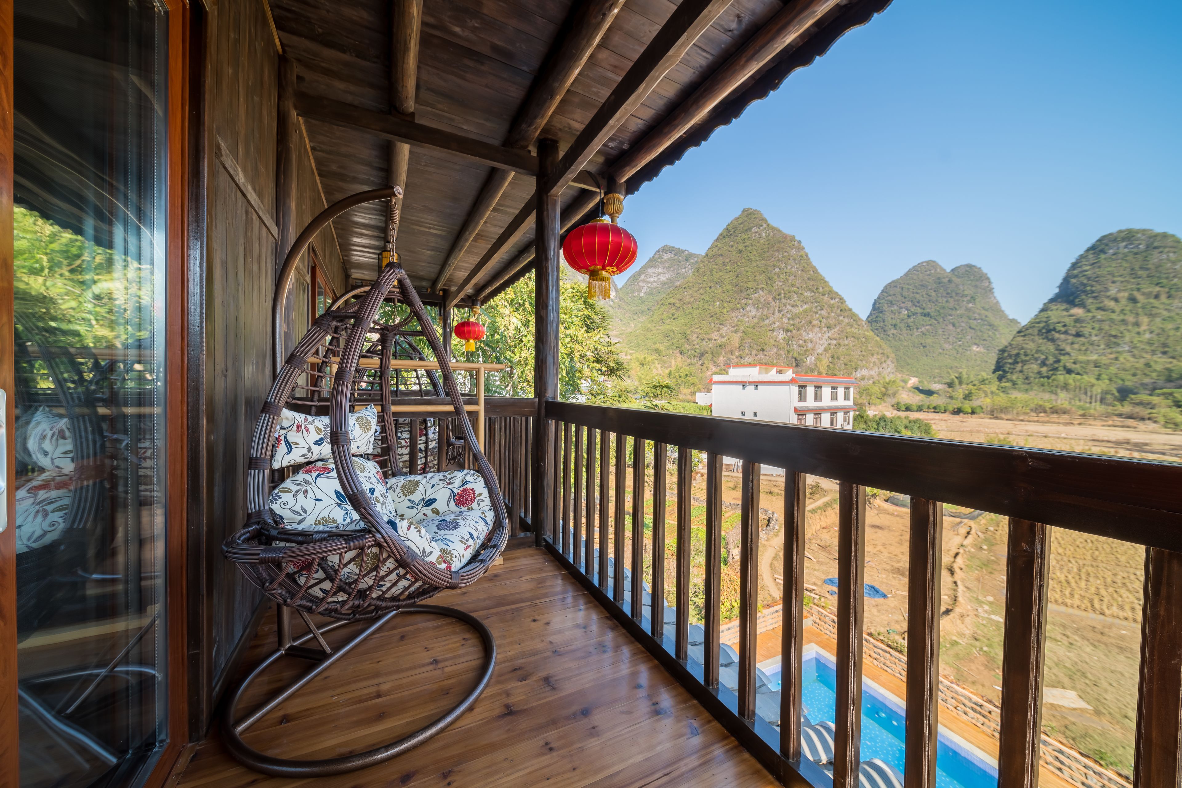 Ein Holzbalkon mit Korbstühlen, Blick auf Berge und ein Schwimmbecken.