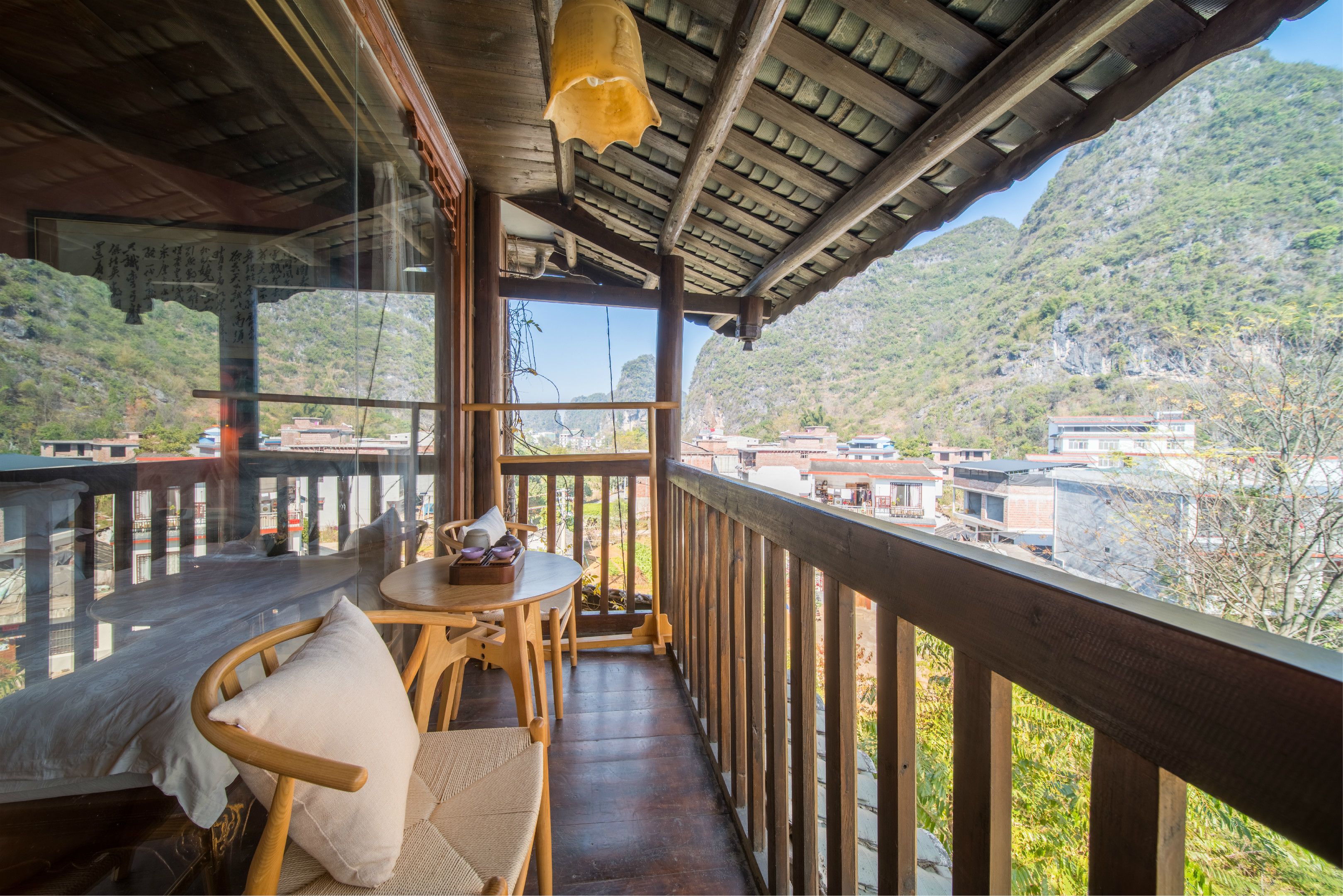 A wooden balcony with a table and chairs, offering a view of a mountainous landscape and buildings in the distance.