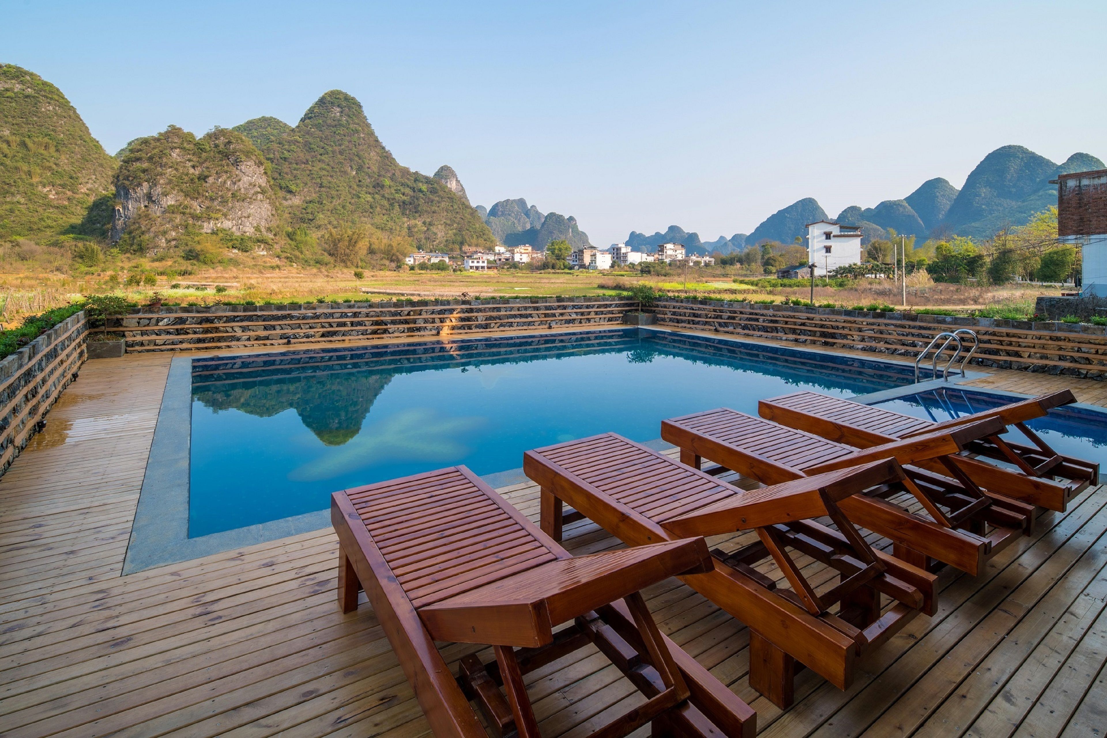 A wooden deck with a pool, lounge chairs, and a view of mountains.