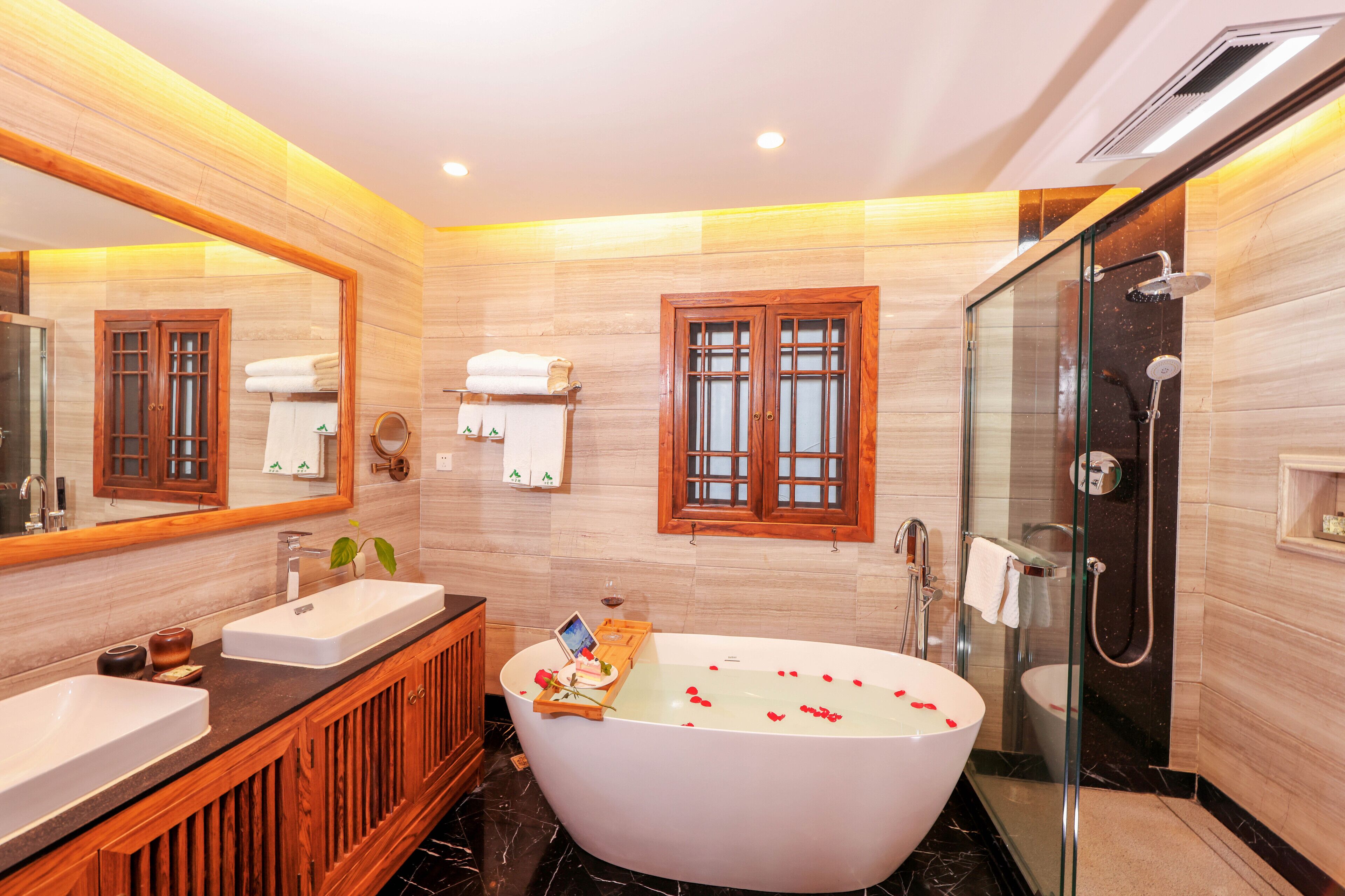 A modern bathroom with a freestanding bathtub, two sinks, a large mirror, and a glass-enclosed shower area.