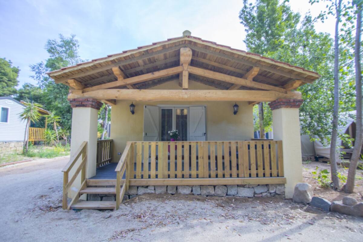 Eine hölzerne Laube mit steinernen Fundament, eine Holzbank und eine Treppe, die hinauf führt.