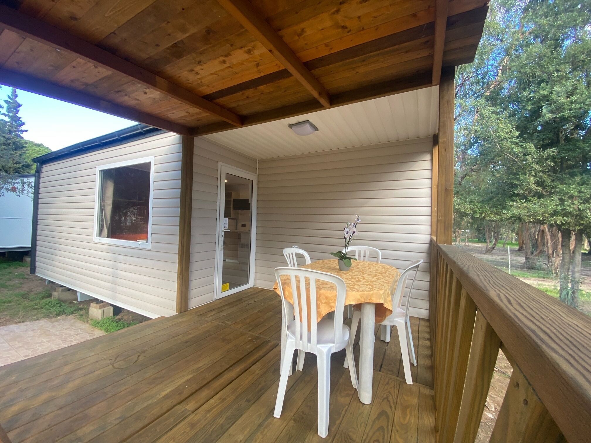 Eine überdachte Veranda mit Holzterrasse, einem Tisch mit Stühlen und einem kleinen Topfpflanzen.