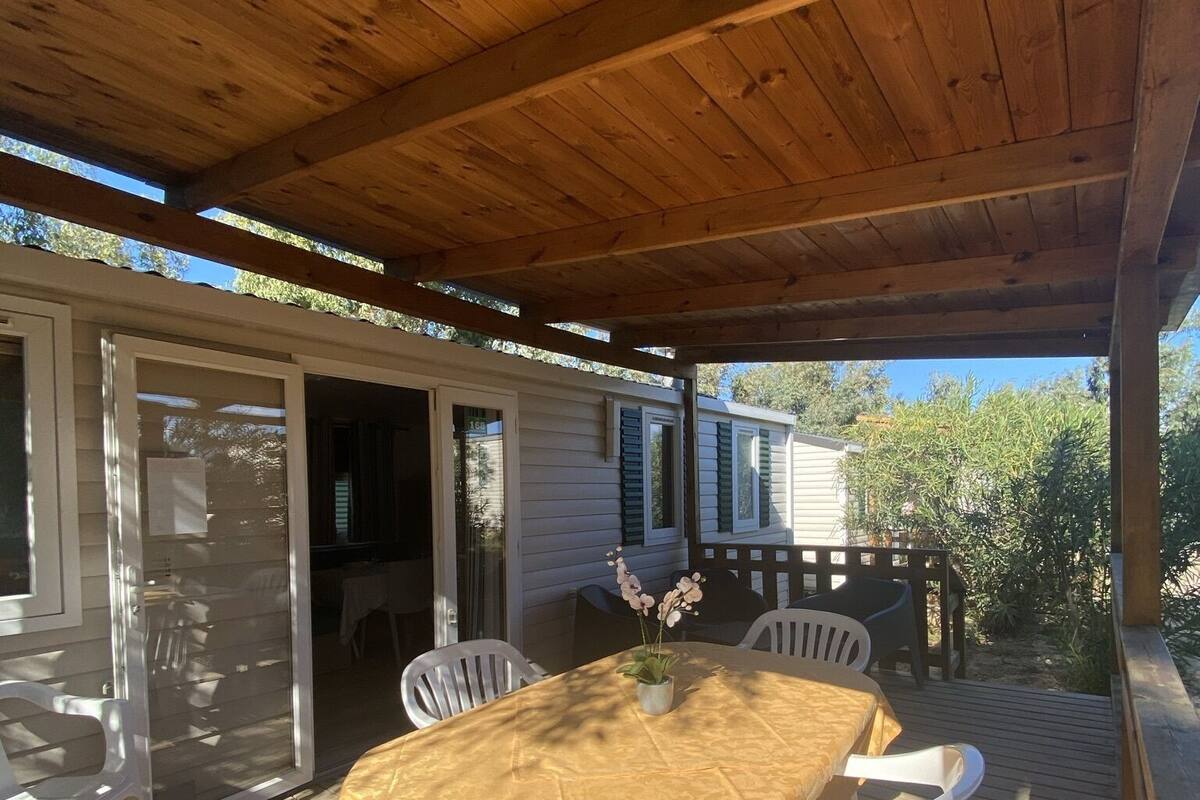 Eine überdachte Terrasse mit Tisch und Stühlen, ein Holzdeck und ein Blick auf ein Haus im Hintergrund.