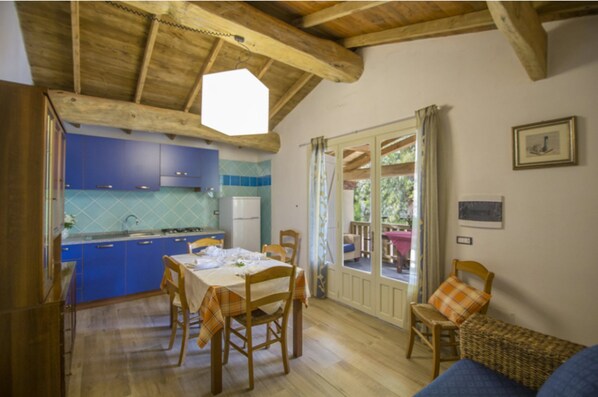 Une cuisine chaleureuse avec des meubles bleus, une table à manger dressée pour quatre personnes et un plafond en bois.