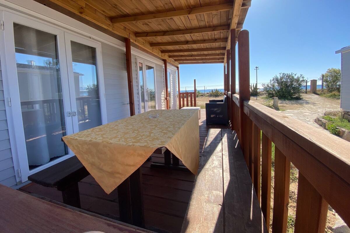 Ein überdachter Außenbereich mit Tisch und Bänken mit Blick auf einen Strand.