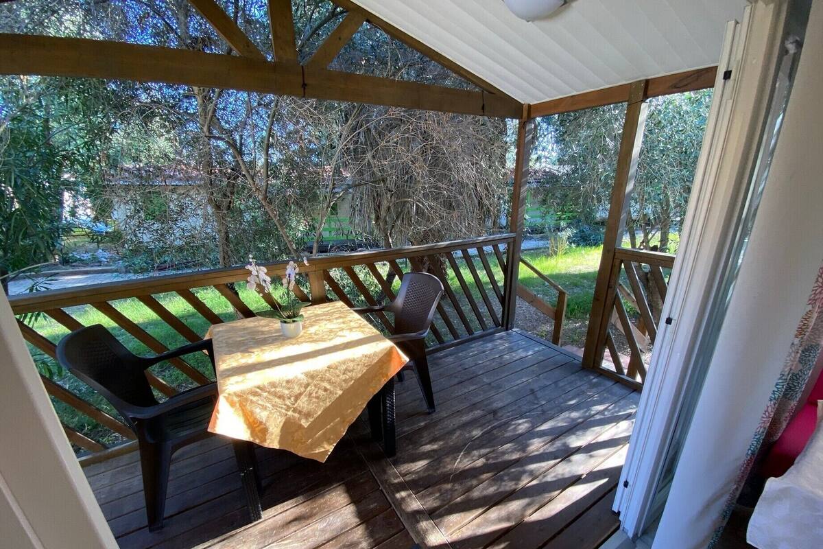 Eine überdachte Terrasse mit Tisch und Stühlen, einem kleinen Topfpflanzen und Blick auf die umliegende Bepflanzung.