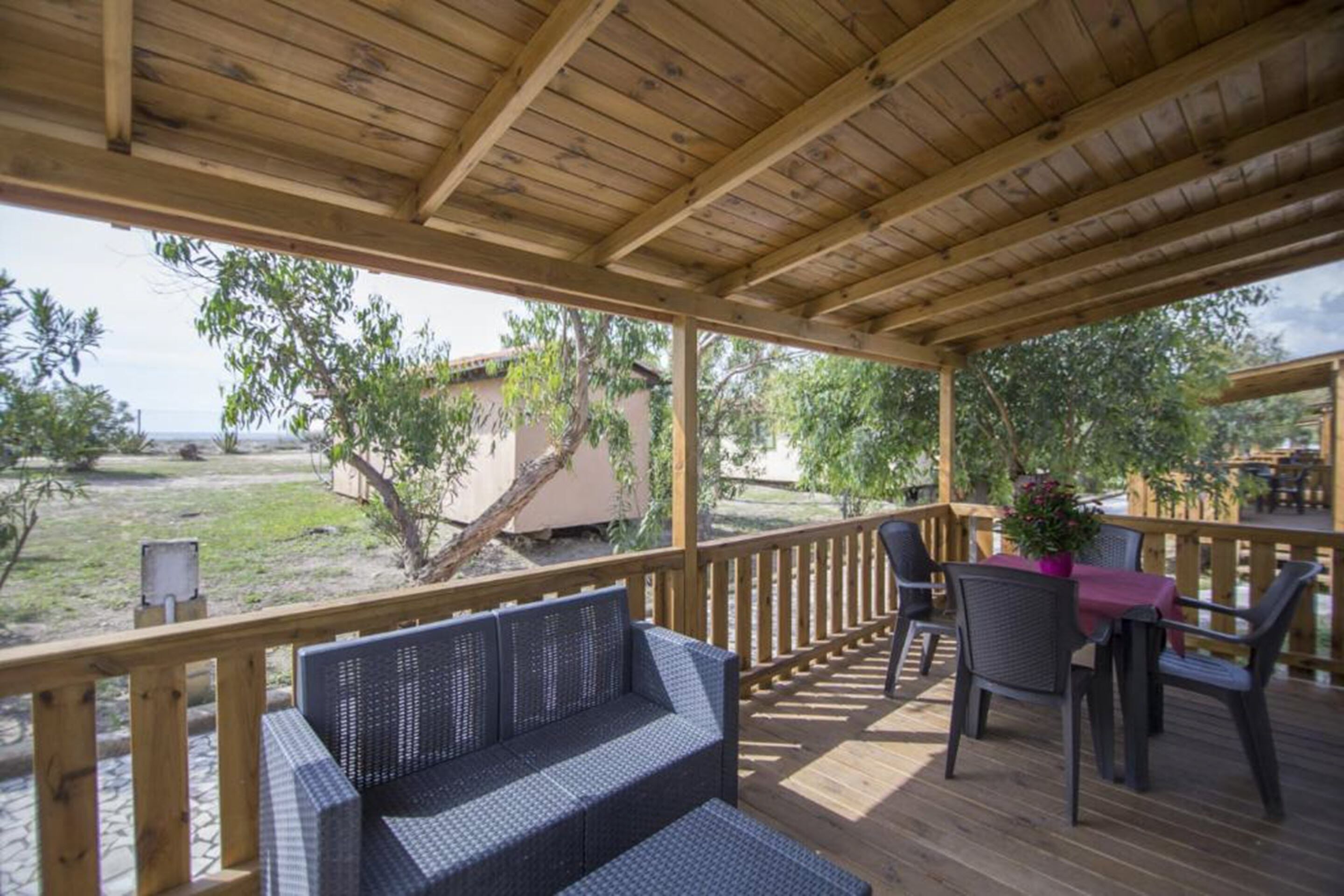 Un espacio al aire libre techado con piso de madera, muebles de mimbre y una mesa con sillas.