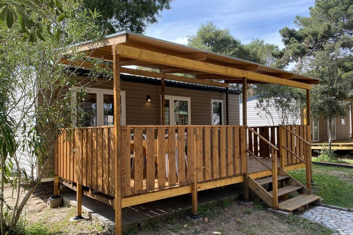 Eine Holzterrasse mit überdachtem Bereich, einer Treppe und einem kleinen Gebäude mit Fenstern.