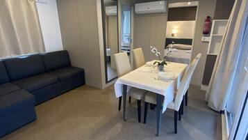 Una sala de estar moderna con un sofá azul oscuro, una mesa de comedor con sillas blancas y una cocina visible a través de un vano abierto.