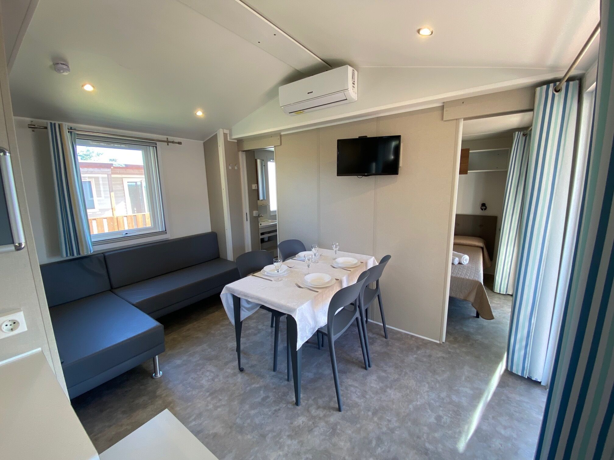 A compact living space with a dining area, a sofa, a TV, and a window with curtains.