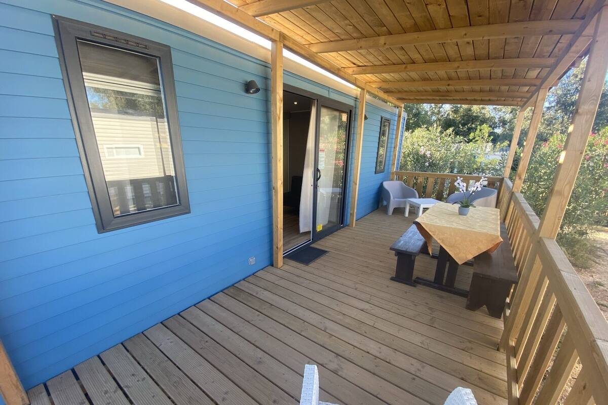 Eine überdachte Terrasse mit Holzboden, einem Tisch mit Stühlen und einer Schiebetür zu einem Innenraum.