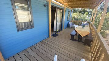 Une terrasse couverte avec un plancher en bois, une table avec des chaises et une porte-fenêtre coulissante donnant sur un espace intérieur.