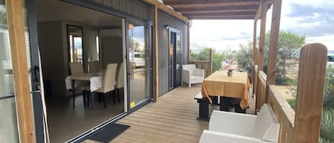 A covered deck with wooden flooring, outdoor seating, and sliding glass doors leading to an interior dining area.