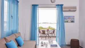 A modern living room with a sofa, a dining table with chairs, and a view of the sea through large windows. - Beach Cabanas (Ermionida)