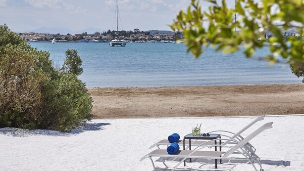 A beach with white sand, a table with two blue towels, and a view of the sea with boats. - Beach Cabanas (Ermionida)