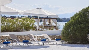 A beachside lounge with sun loungers and umbrellas, overlooking a body of water and mountains. - Beach Cabanas (Ermionida)
