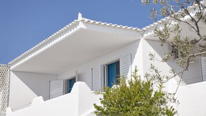 A white building with a balcony, a tree in the foreground, and a clear blue sky. - Beach Cabanas (Ermionida)