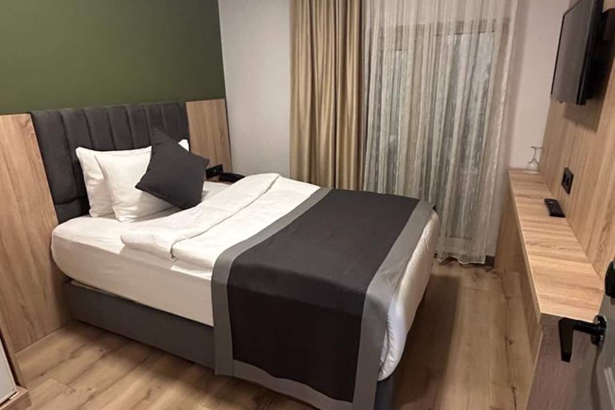 A modern bedroom with a bed, wooden headboard, and a TV on the wall.