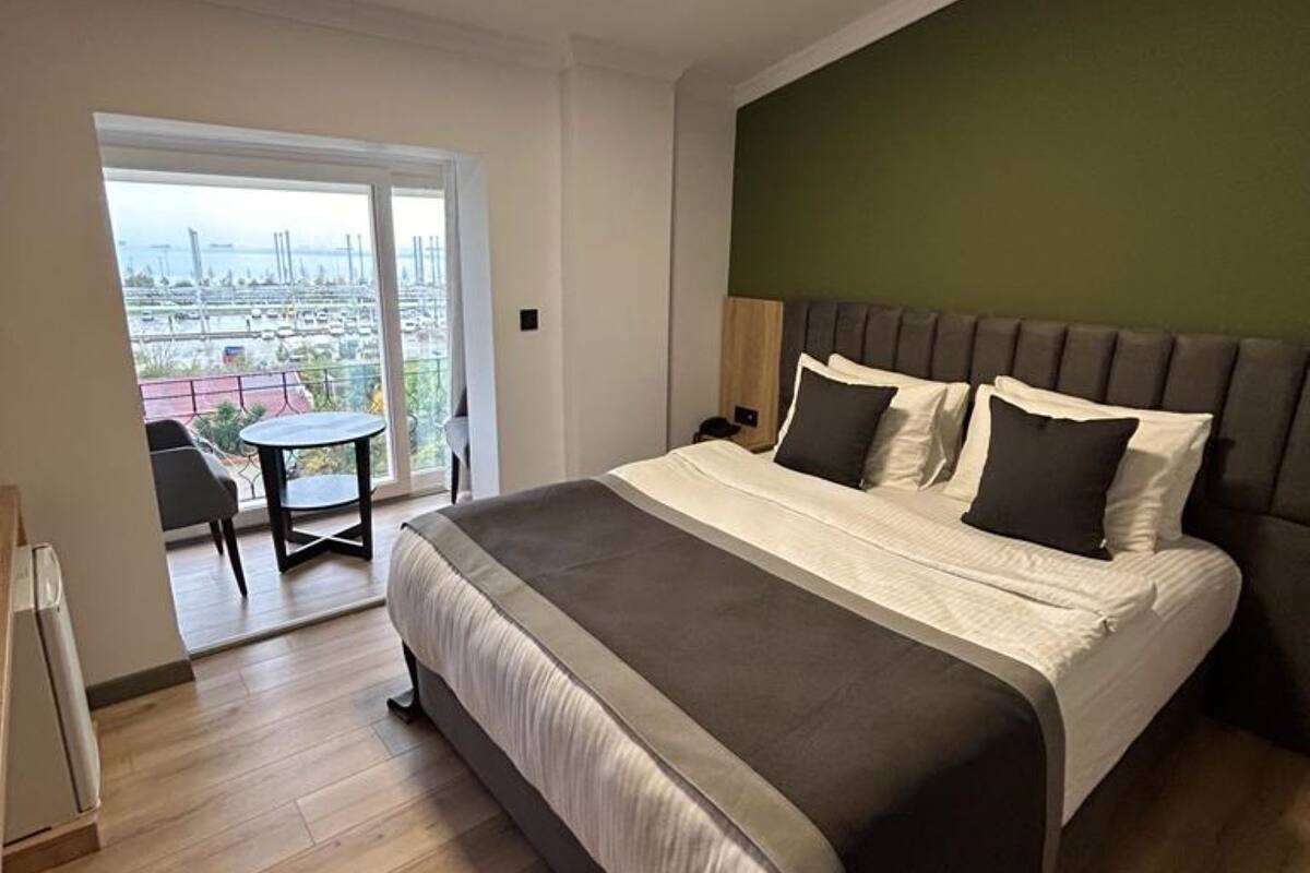 A modern bedroom with a large bed, a view of a marina, and a balcony with a table and chairs.