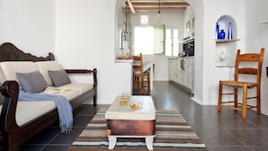A living room with a sofa, a wooden coffee table, a striped rug, and a kitchen in the background. - Skaris Homes (Tinos)